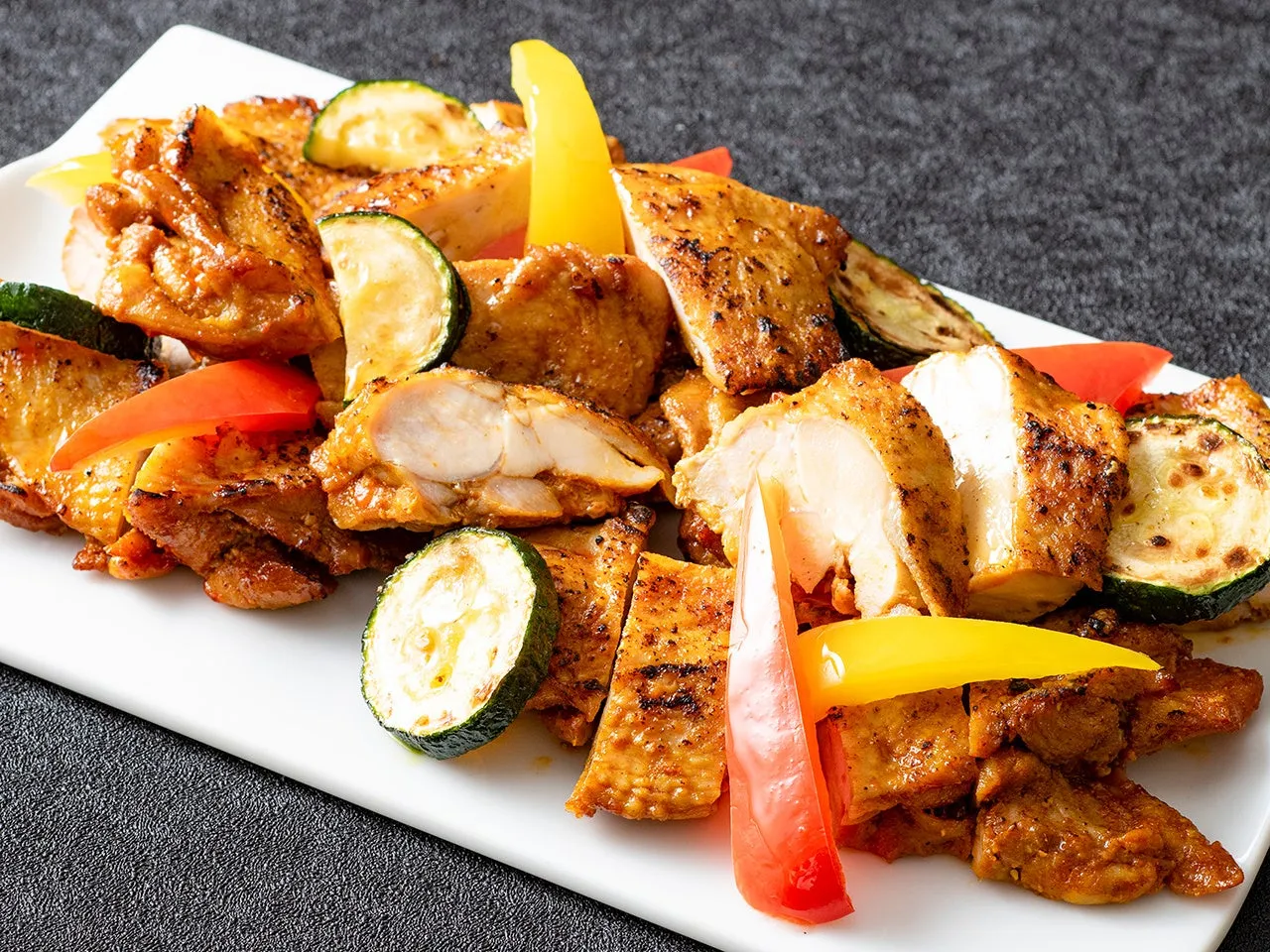 焼き鳥と野菜の盛り合わせが白い皿に盛られた料理の写真です。鶏肉は焼き色が付いており、ズッキーニやパプリカなどの野菜が添えられています。